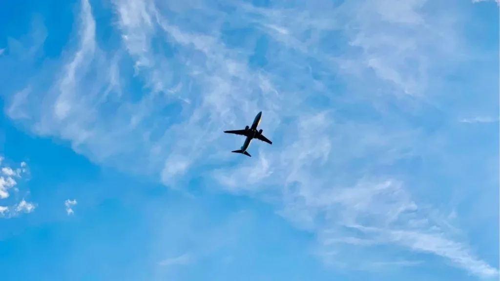 Contrat de régulation économique d’ADP : le SCARA monte au créneau Un avion de ligne en contre‑jour survole un vaste ciel bleu strié de nuages fins, évoquant le voyage et le mouvement.
