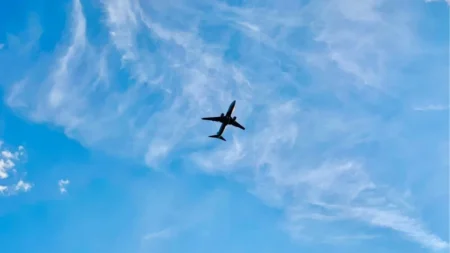 Un avion de ligne en contre‑jour survole un vaste ciel bleu strié de nuages fins, évoquant le voyage et le mouvement.